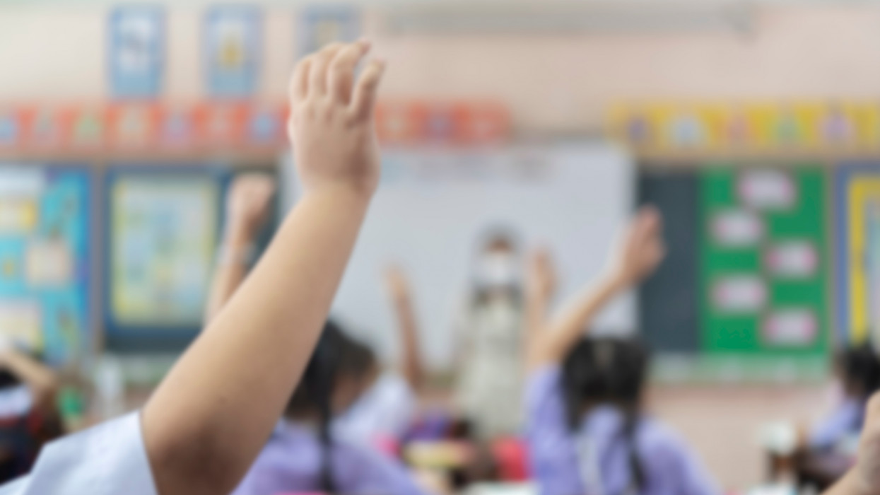 Blurred of elementary school student is raising their hands to ask the teacher standing in front of the class.