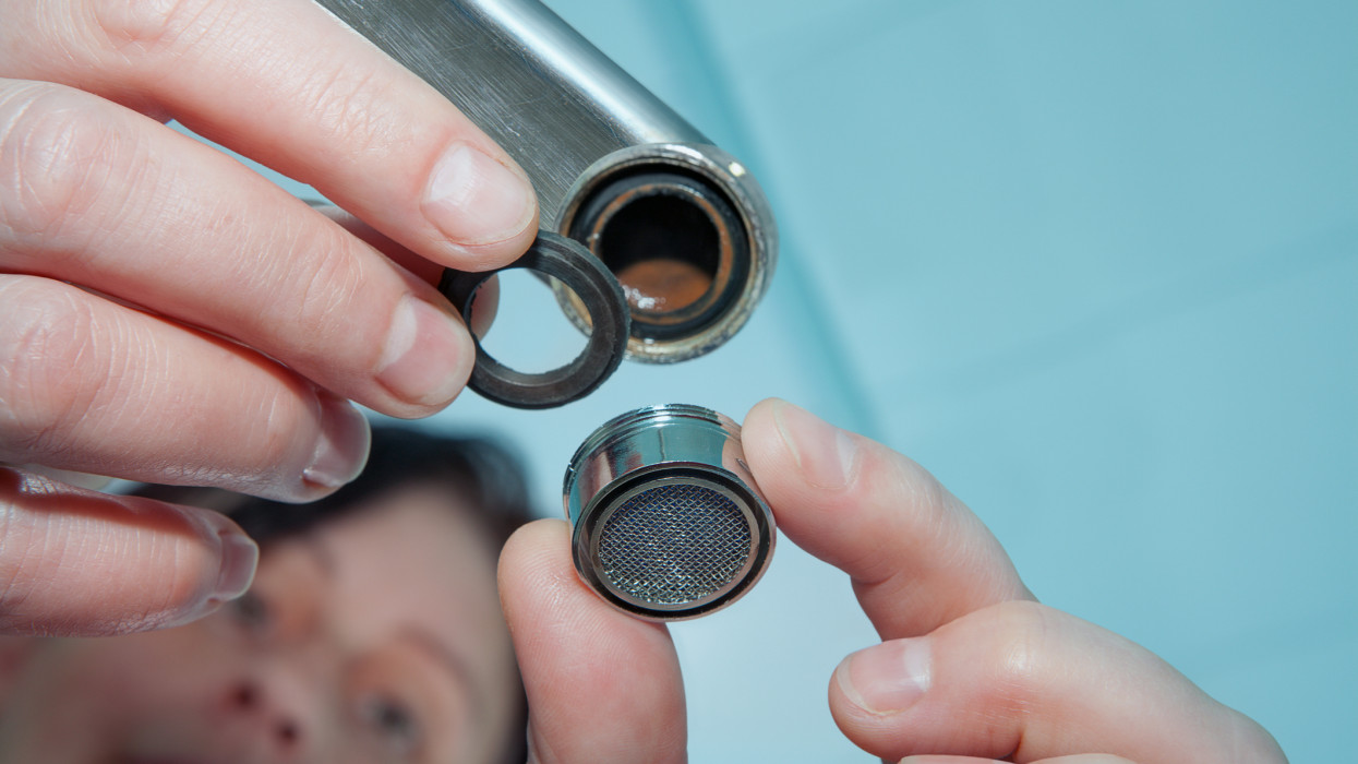 Woman plumber installing faucet aerator,  close-up of hand handyman repairing a tap in the bathroom.