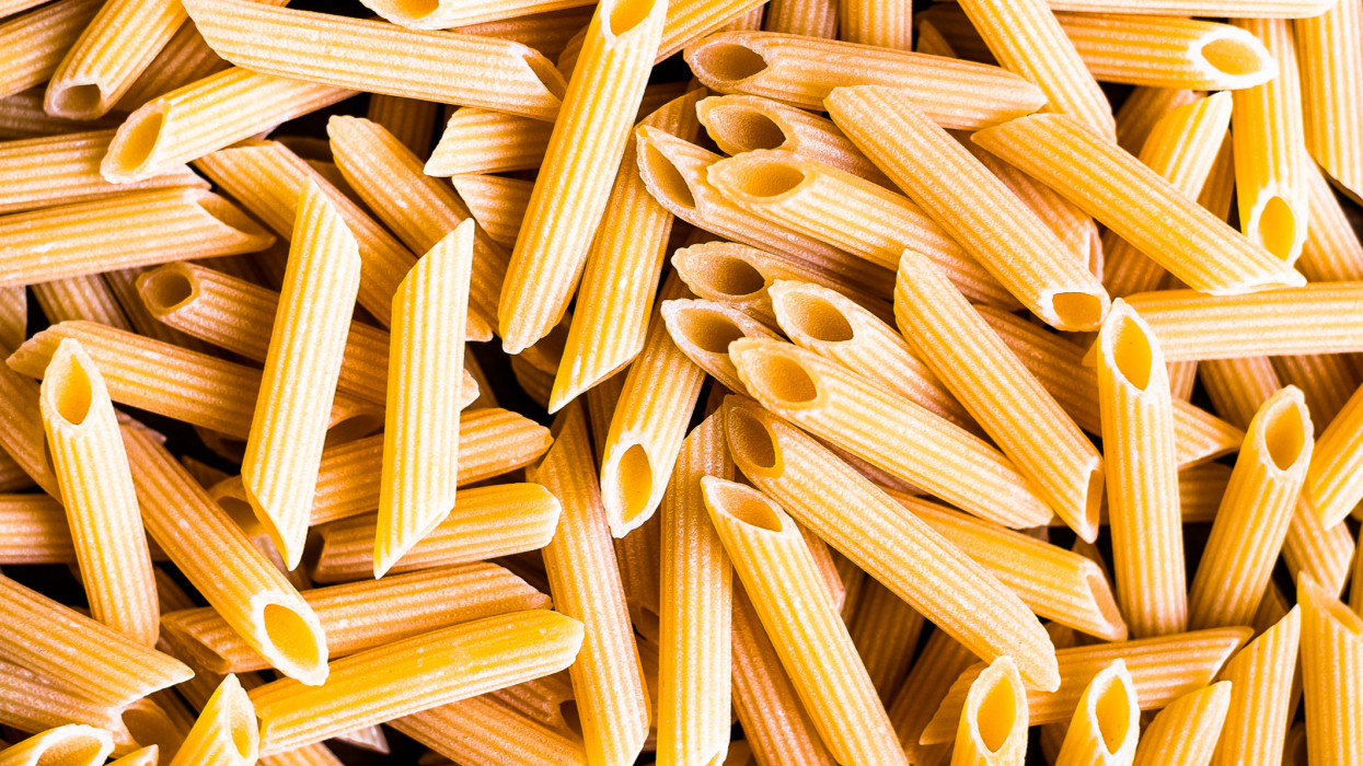 Heap of uncooked whole wheat penne italian pasta, top view. Pasta pattern. Food background.
