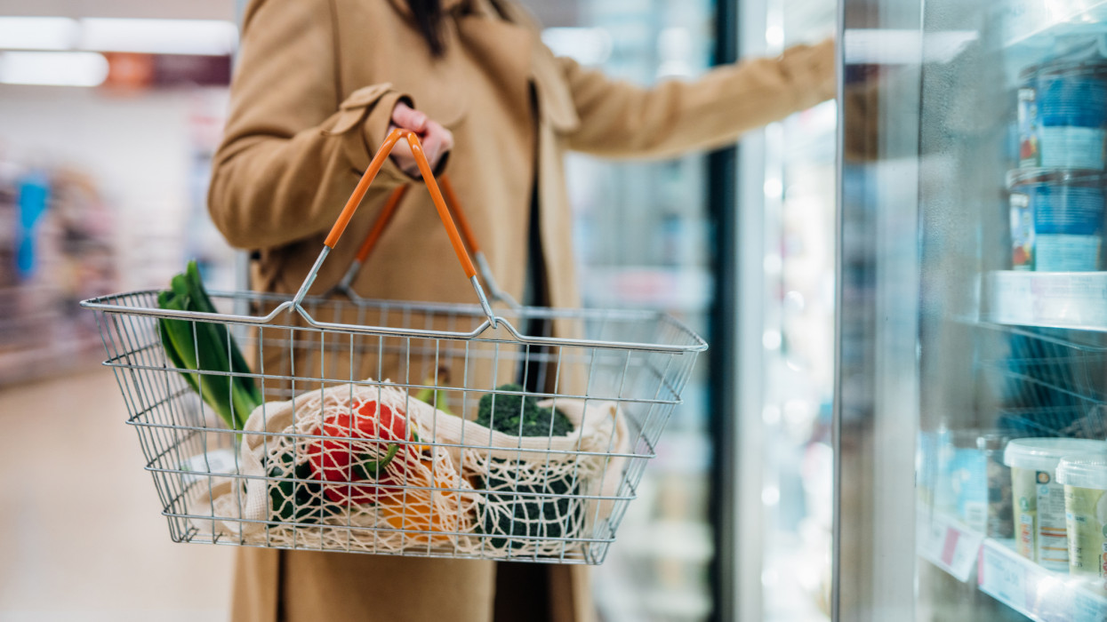 Close up shot of woman carrying shopping basket and shopping groceries in supermarket. City solo life concept. Single person.