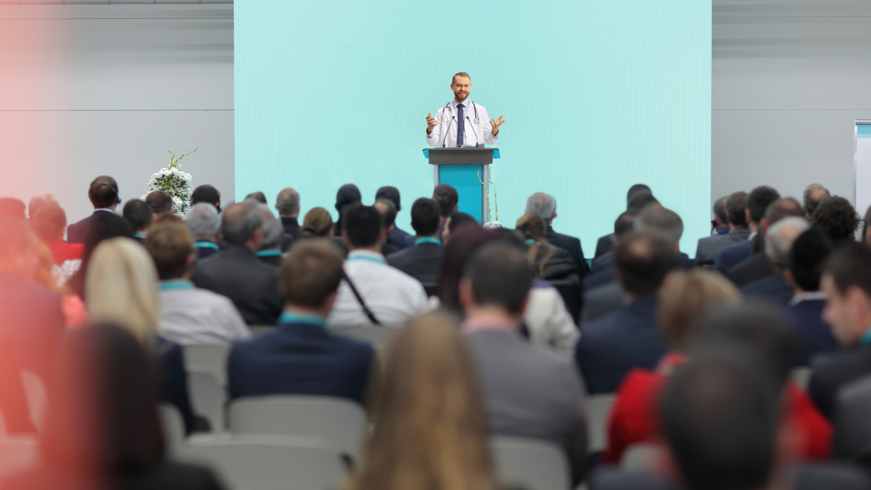 Male doctor giving a speech on a podium at a conference in front of an audience
