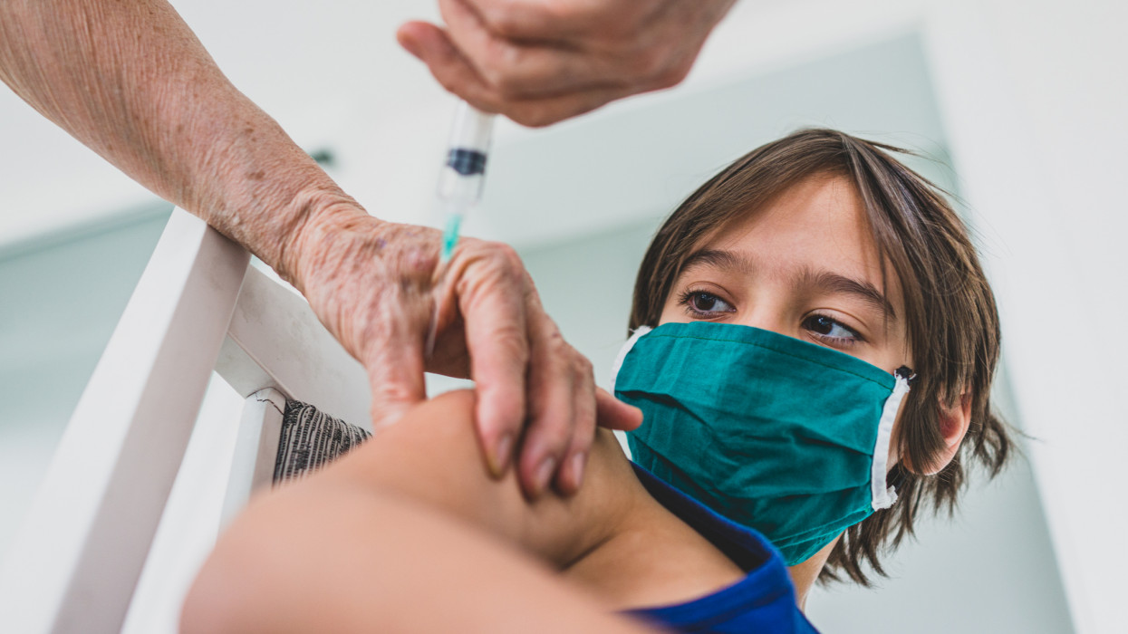 Child wearing mask getting vaccinated by doctor holding a needle