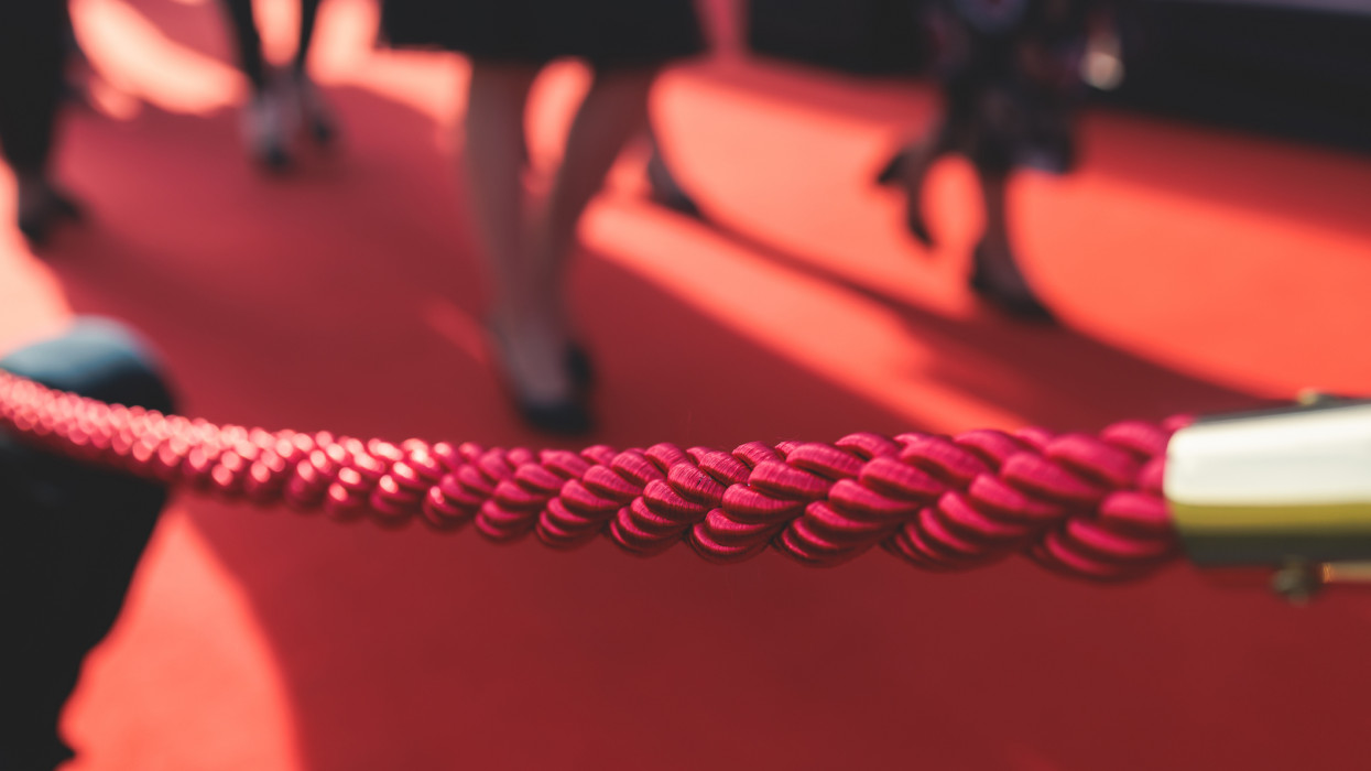 Red carpet with the ropes and golden barriers on a luxury party entrance, cinema premiere film festival event gala ceremony, wealthy rich guests ariving, outdoor decoration elements, summer sunny day