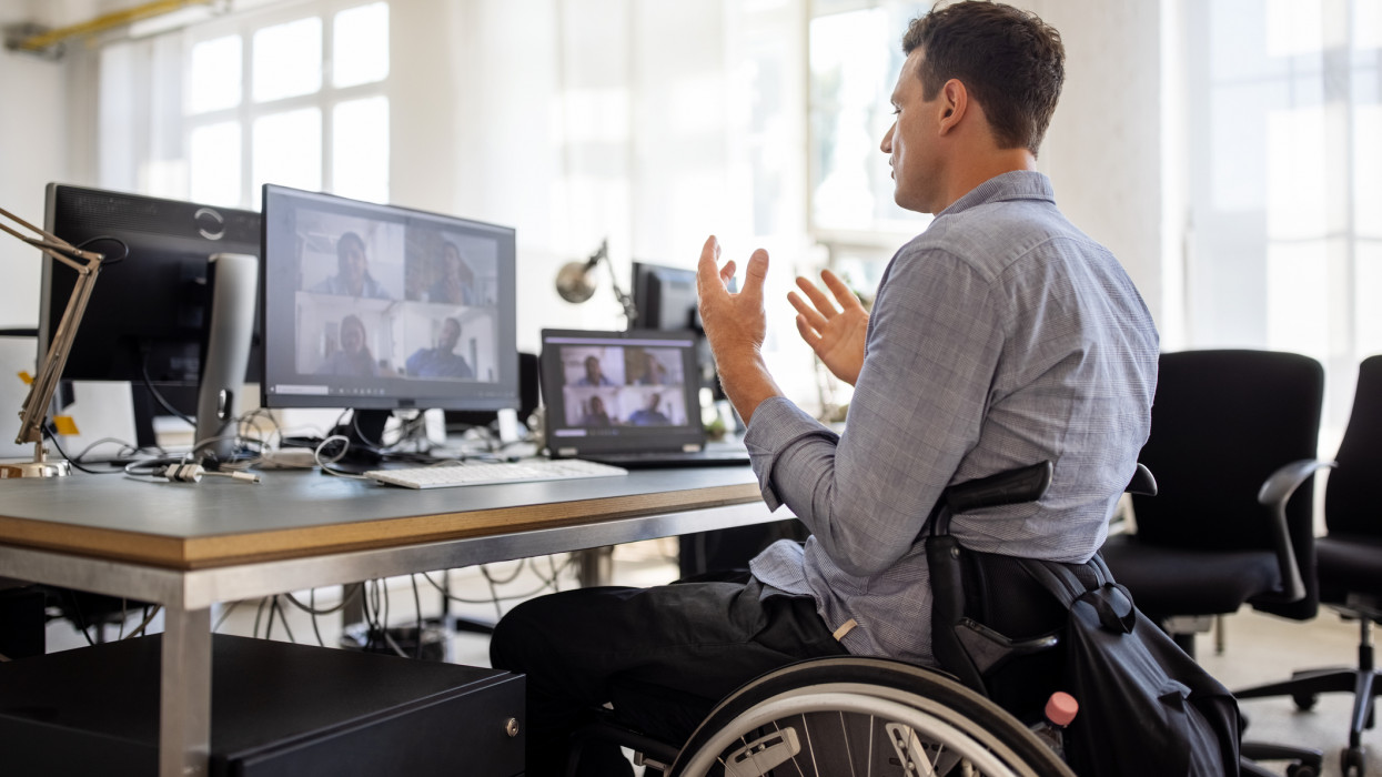Businessman with disability talking on video call at office. Businessman on a wheelchair having a web conference on his computer at creative office desk.
