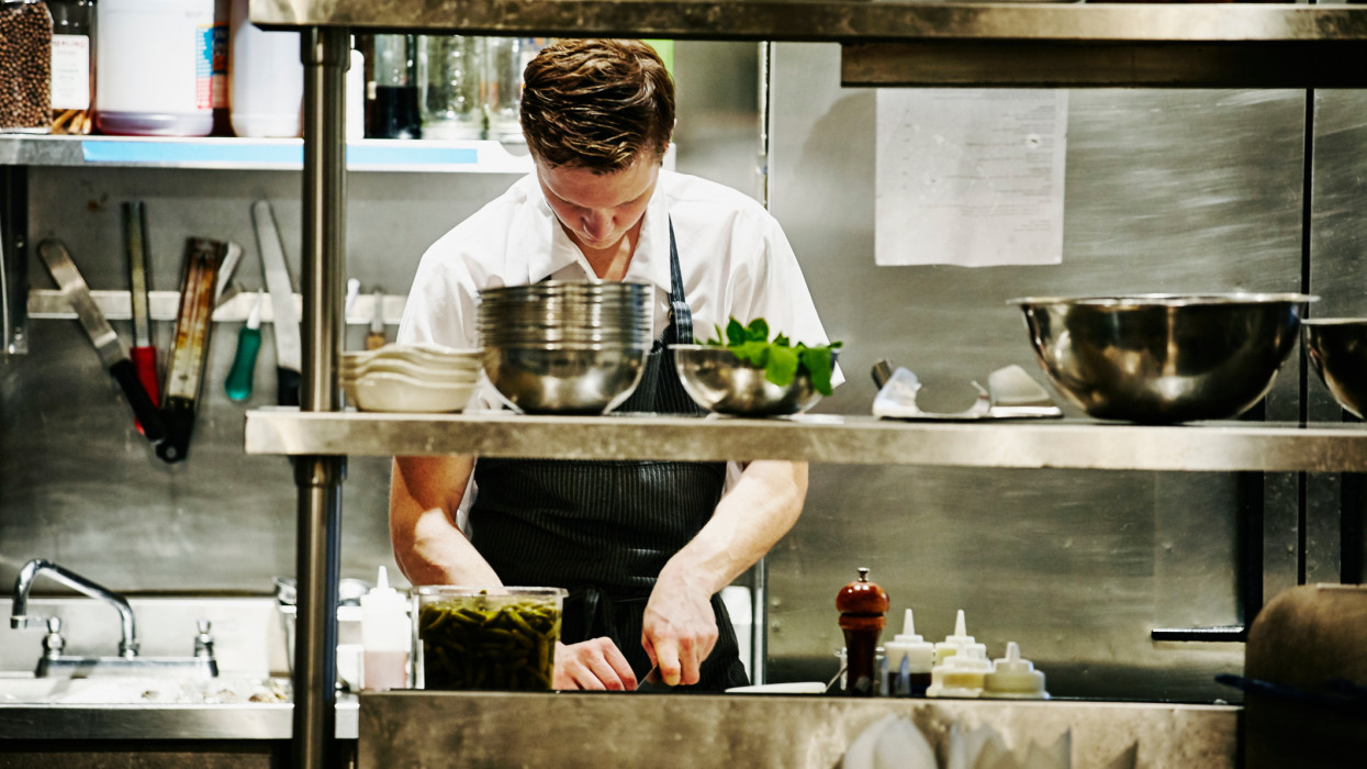 Sous chef chopping ingredients for dinner service at workstation in restaurant kitchen