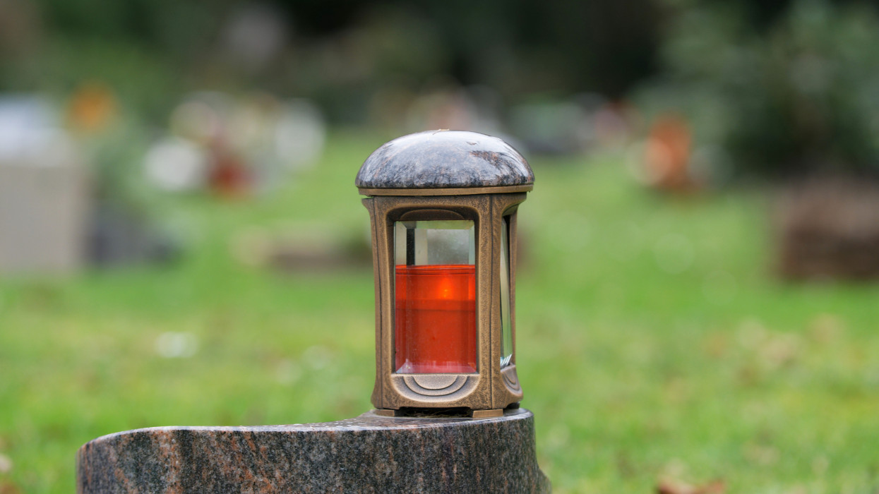 metal grave lantern on a marble pedestal in front of graves in blurred background