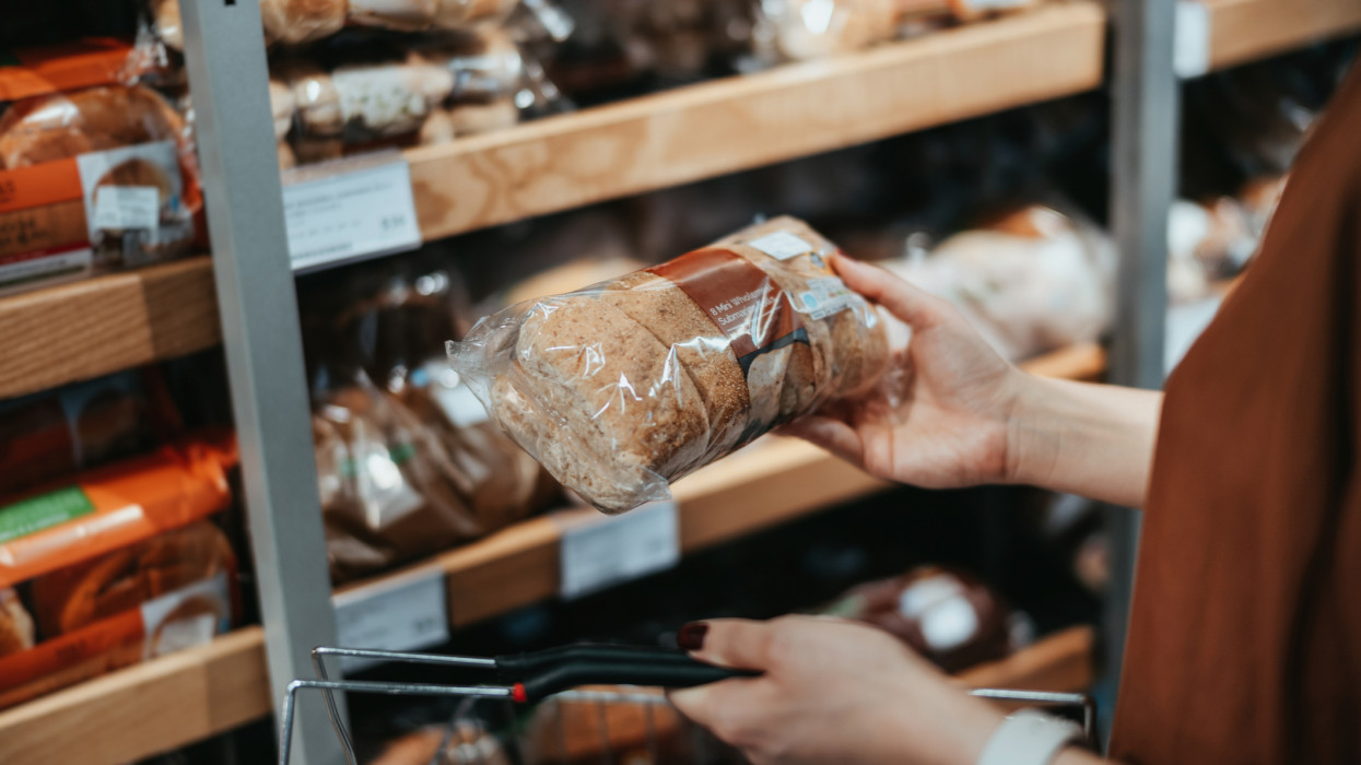 Young Asian woman carrying a shopping basket grocery shopping in a supermarket, shopping for packaged fresh wholegrain bread in the bread aisle. Healthy eating lifestyle