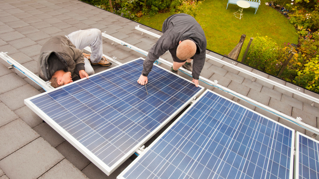 Technicians fitting solar photo voltaic panels to a house roof in Ambleside, Cumbria, UK.
