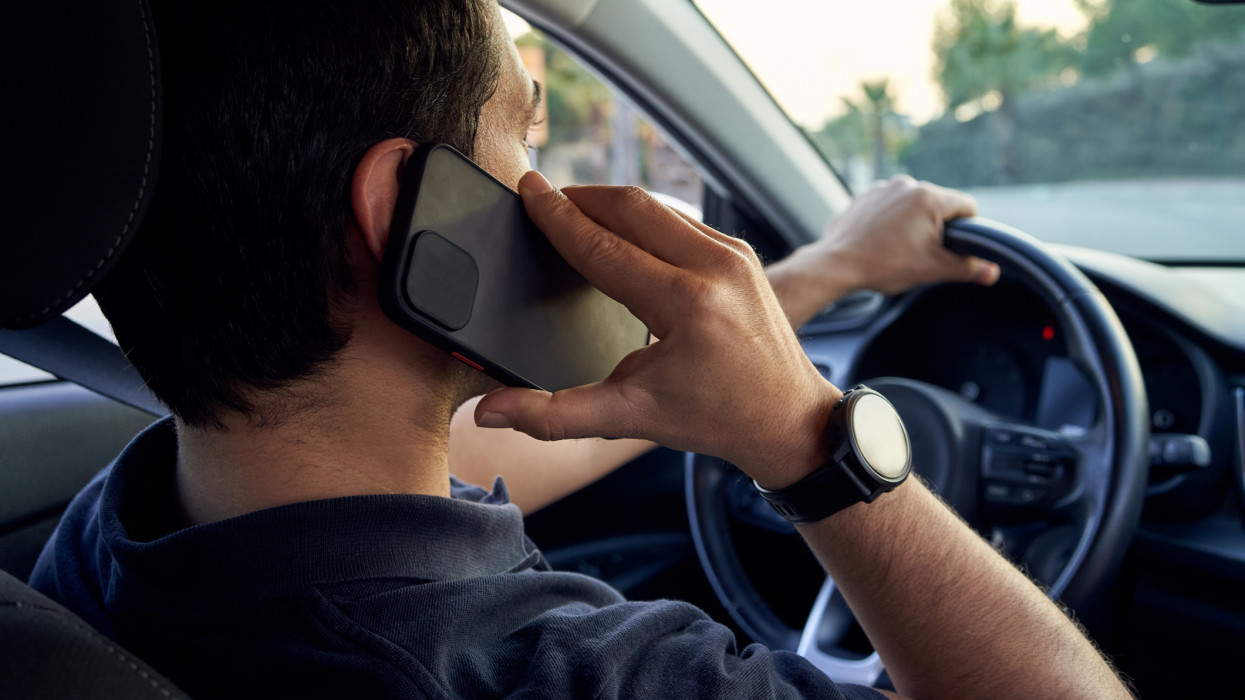 Rear view of a young unrecognizable Hispanic man talking on a smartphone while driving his car. Concept of driving and road safety.