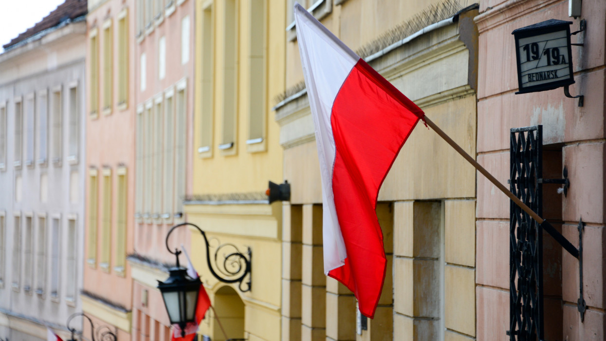 The national flag of Poland displayed on poles outside traditional buildings in the old town of Warsaw