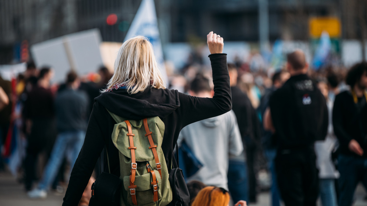 Young woman with a raised fist protesting in the street in front of the government building.2021