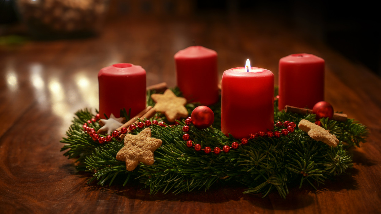 First Advent - decorated Advent wreath from fir branches with red burning candles on a wooden table in the time before Christmas, festive bokeh in the warm dark background, copy space, selected focus