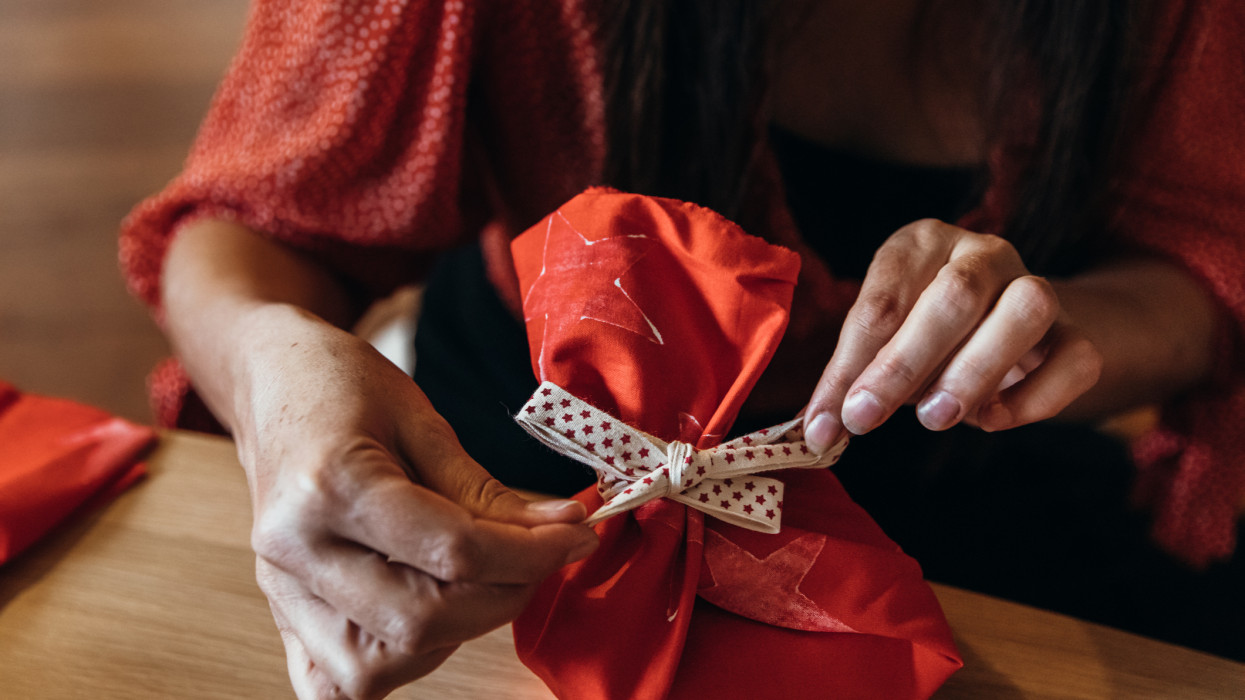 Young Australian mum wraps presents in reusable homemade fabric wrap and ribbon with Christmas tree and gifts in the background
