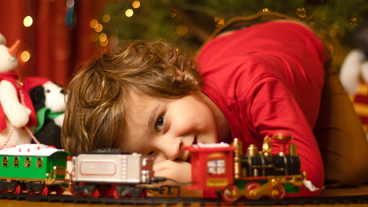 Photo of 4-year smiling boy playing toy train . Christmas tree with Christmas lights illumination.  Soft defocused