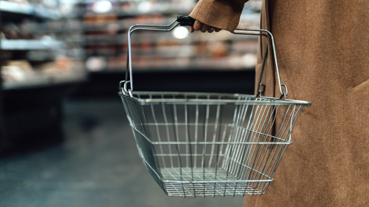 Close up shot of woman carrying empty shopping basket in supermarket.