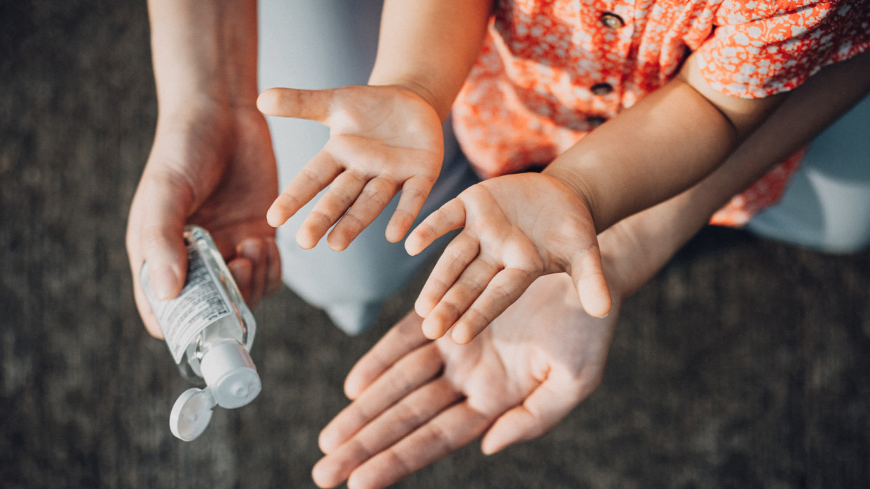 Mother squeezing hand sanitizer onto little daughters hand outdoors to prevent the spread of viruses during the Covid-19 health crisis