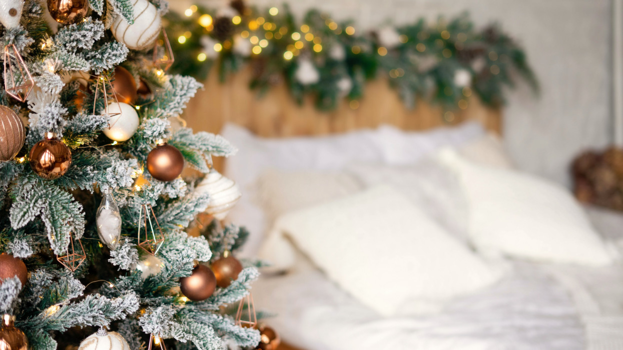 Decorated Christmas bedroom with Christmas tree. Light Scandinavian interior. Cozy bed in a chalet.