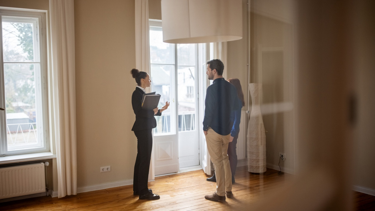 Full length of businesswoman discussing with customers at empty home. Female Real Estate Agent is standing with man and woman by window. They are at new apartment.