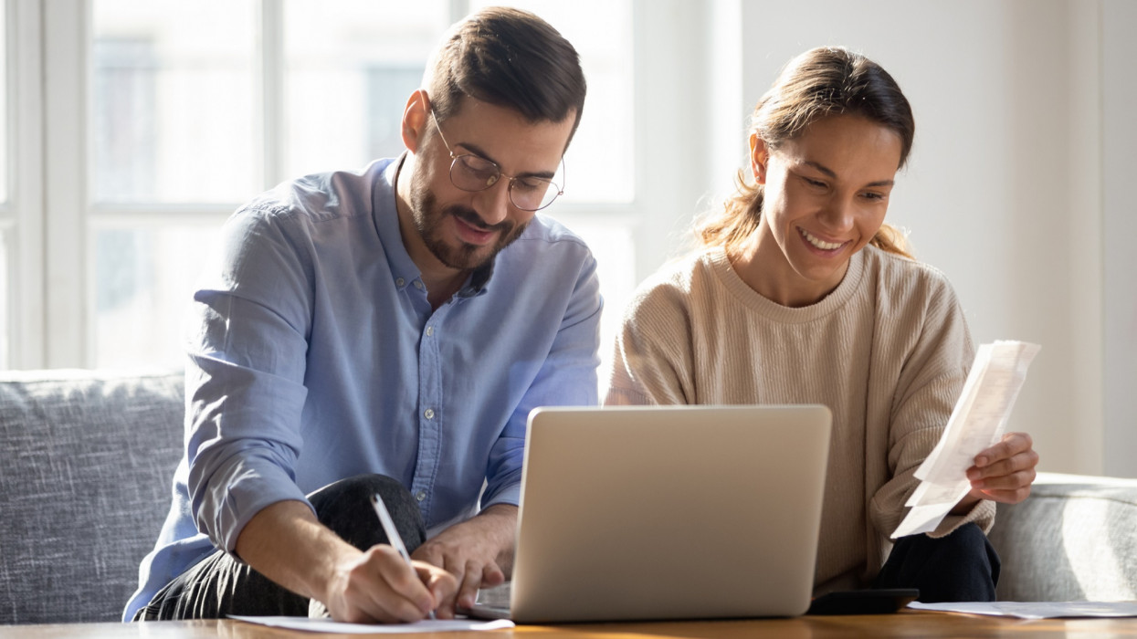 Happy couple using laptop, calculating domestic bills, mortgage or loan documents, smiling woman holding papers, family planning budget, managing household expenses, focused man filling form