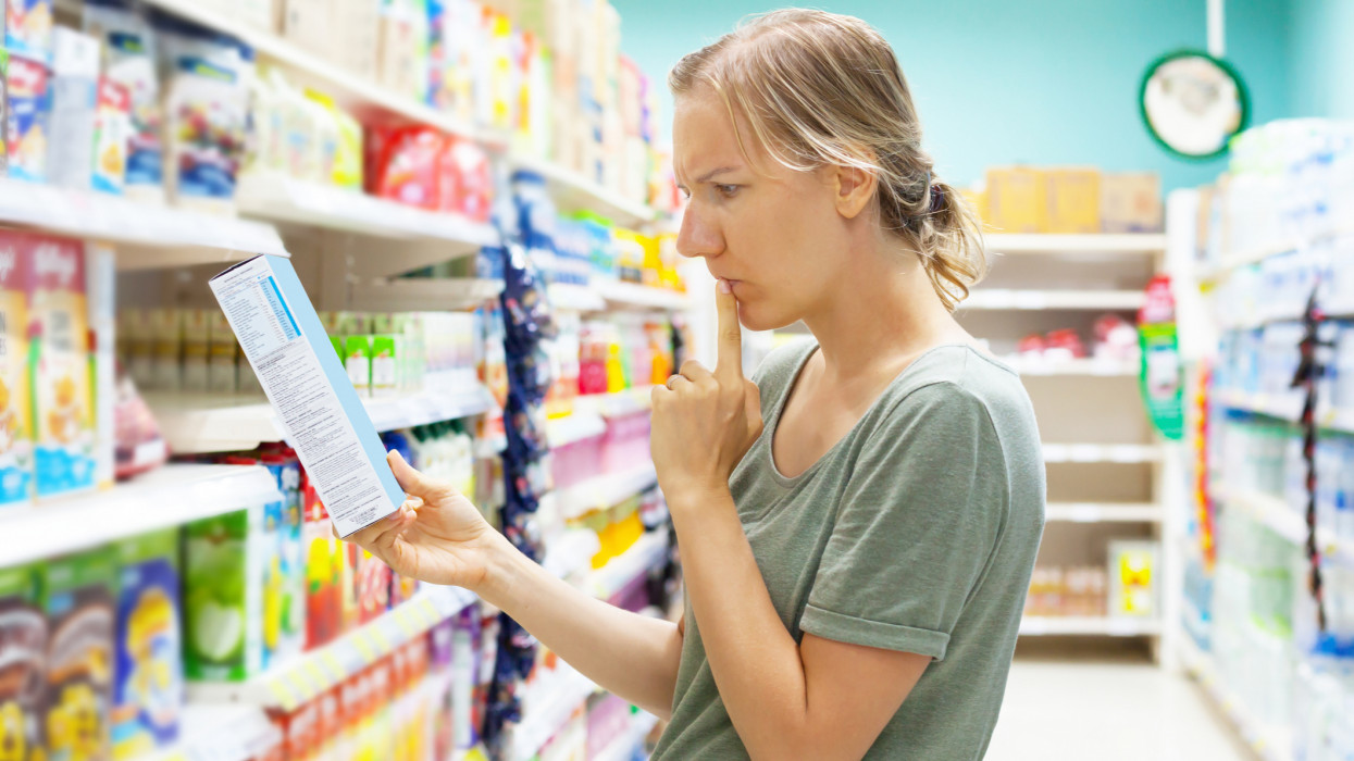 Young woman in supermarket groceries carefully reading nutrients of cornflakes quick breakfast. Healthy eating concept