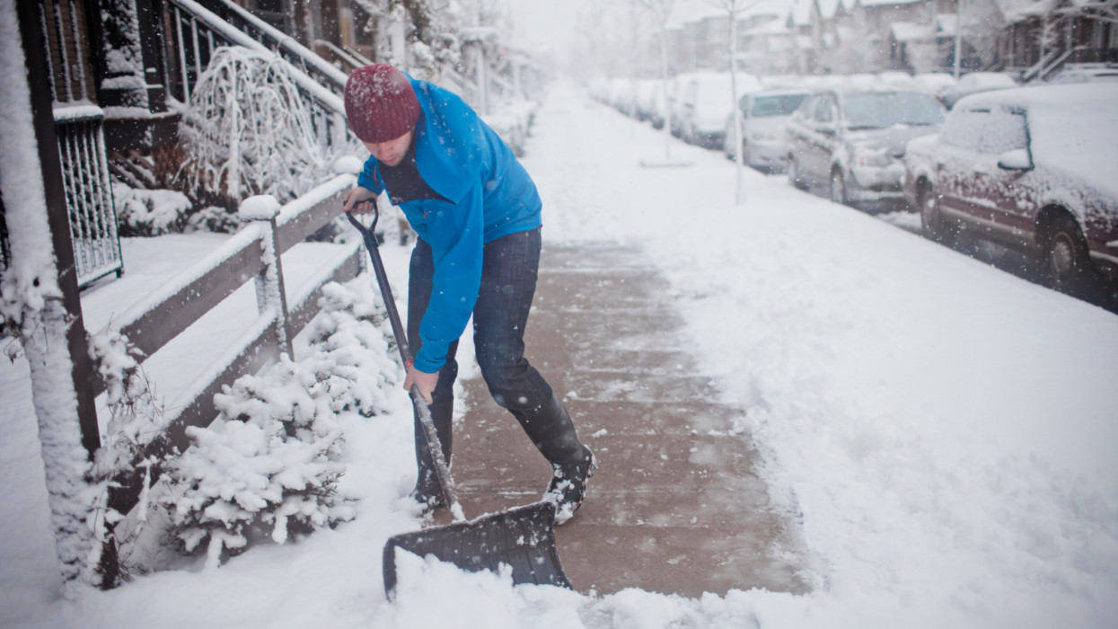 A man shovels the sidewalk outside of his suburban house during a snow storm.
