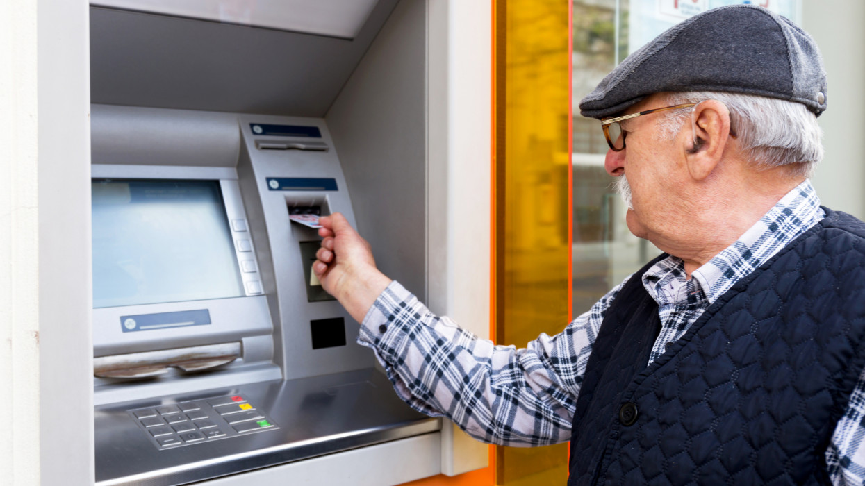 elderly man inserting credit card to ATM outdoor