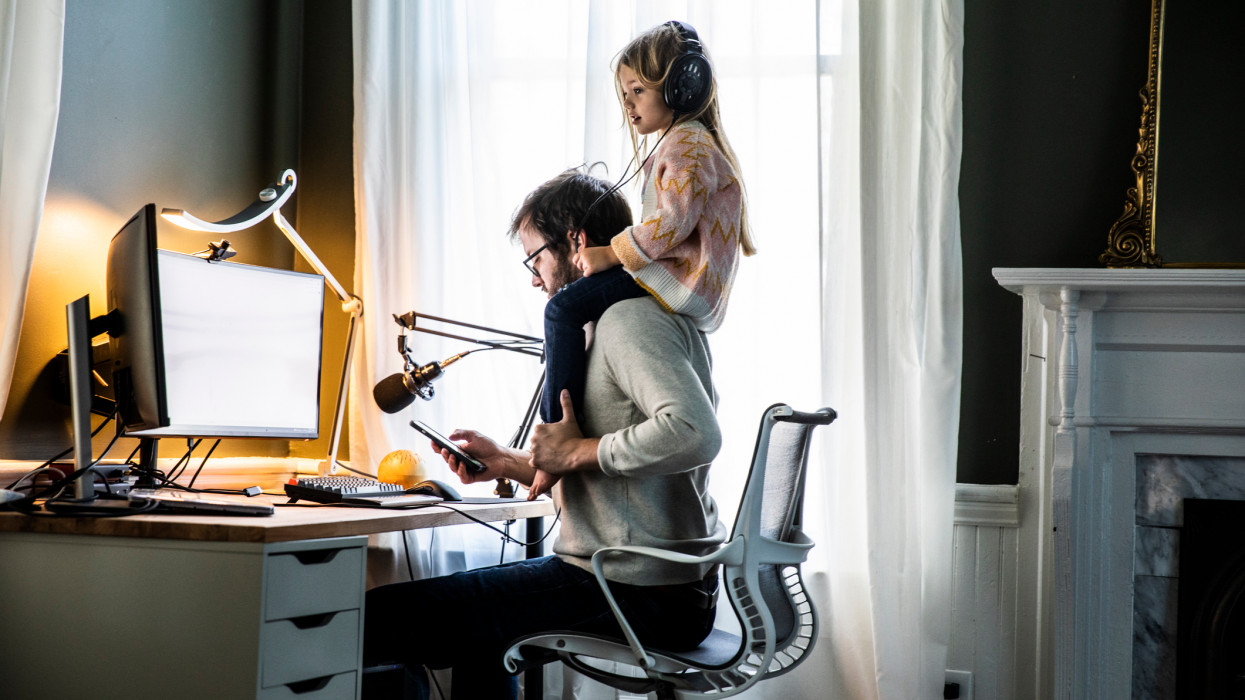 Father working in home office with  young daughter on shoulders