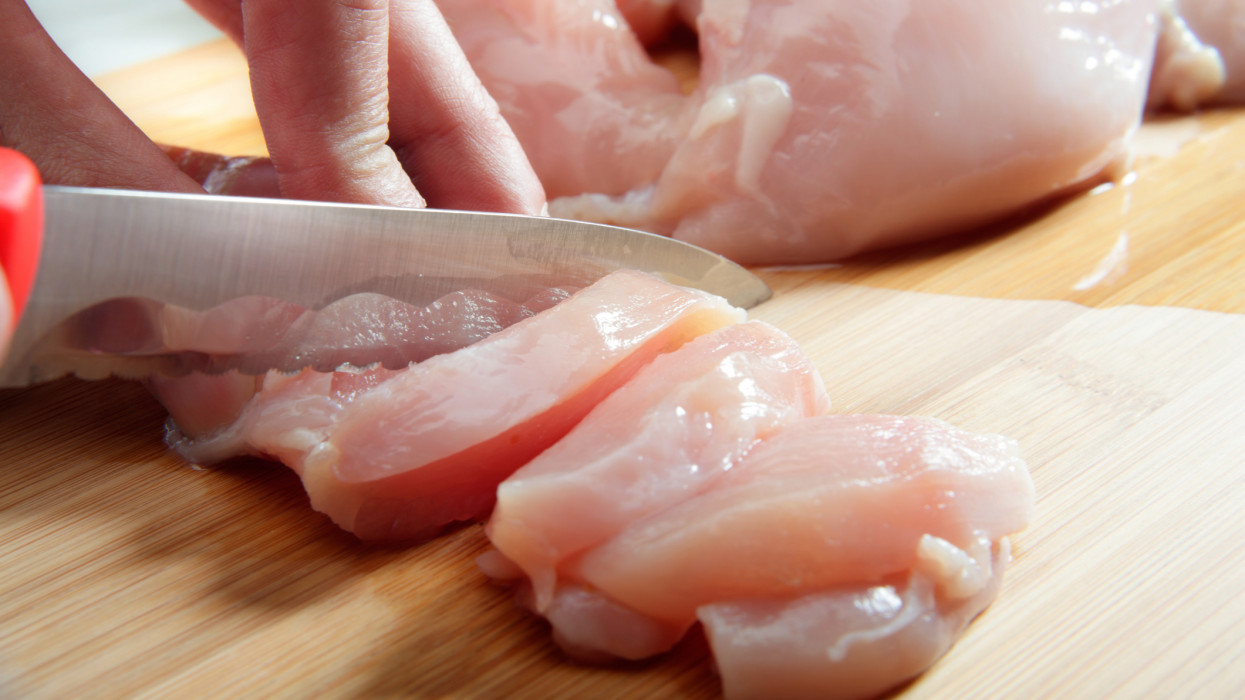 Mans hand cutting raw chicken breast. Selective focus