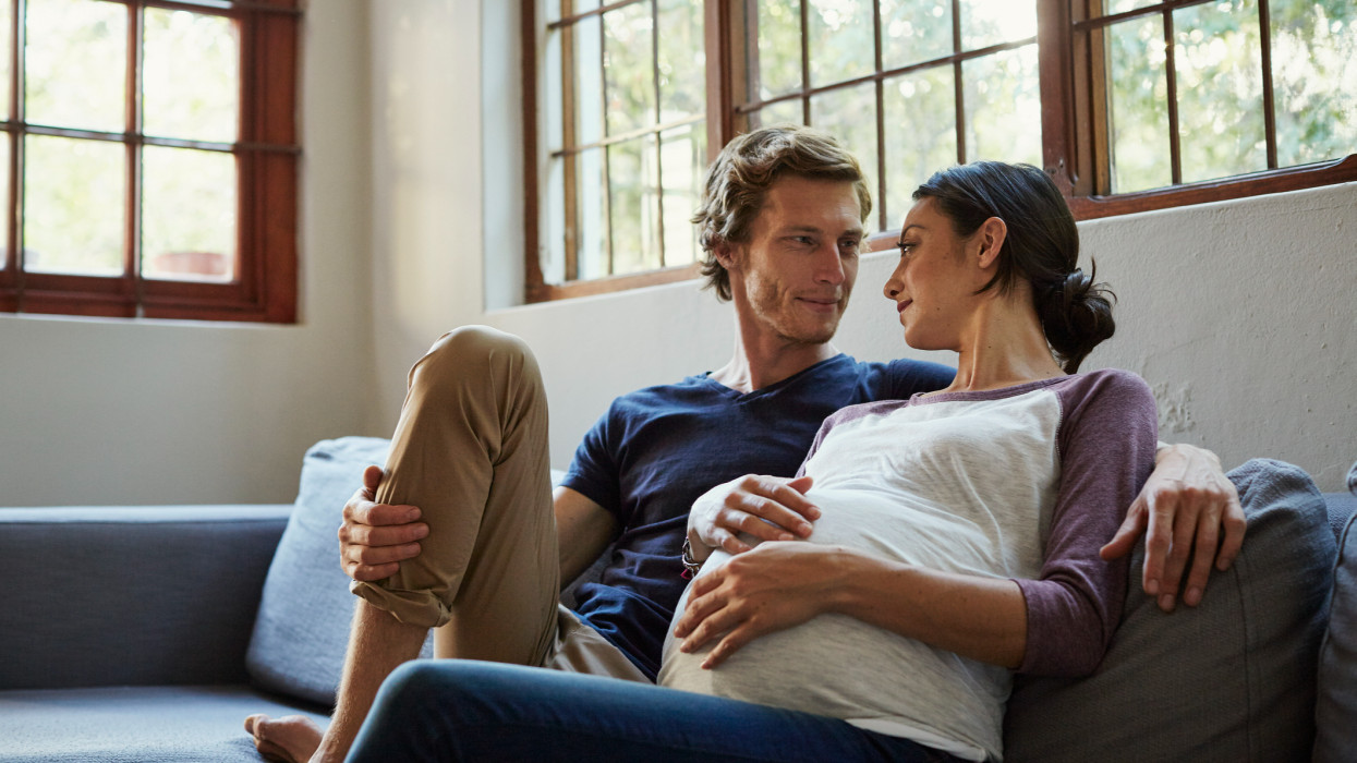 Loving expectant couple looking at each other while relaxing on sofa