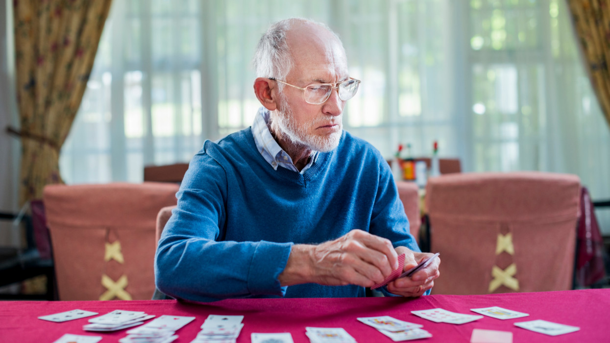 Senior man playing cards at table in nursing home