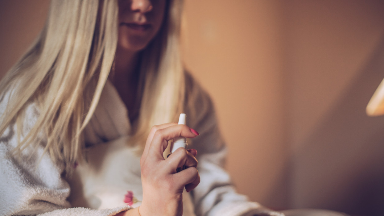 Sick young woman using nasal spray