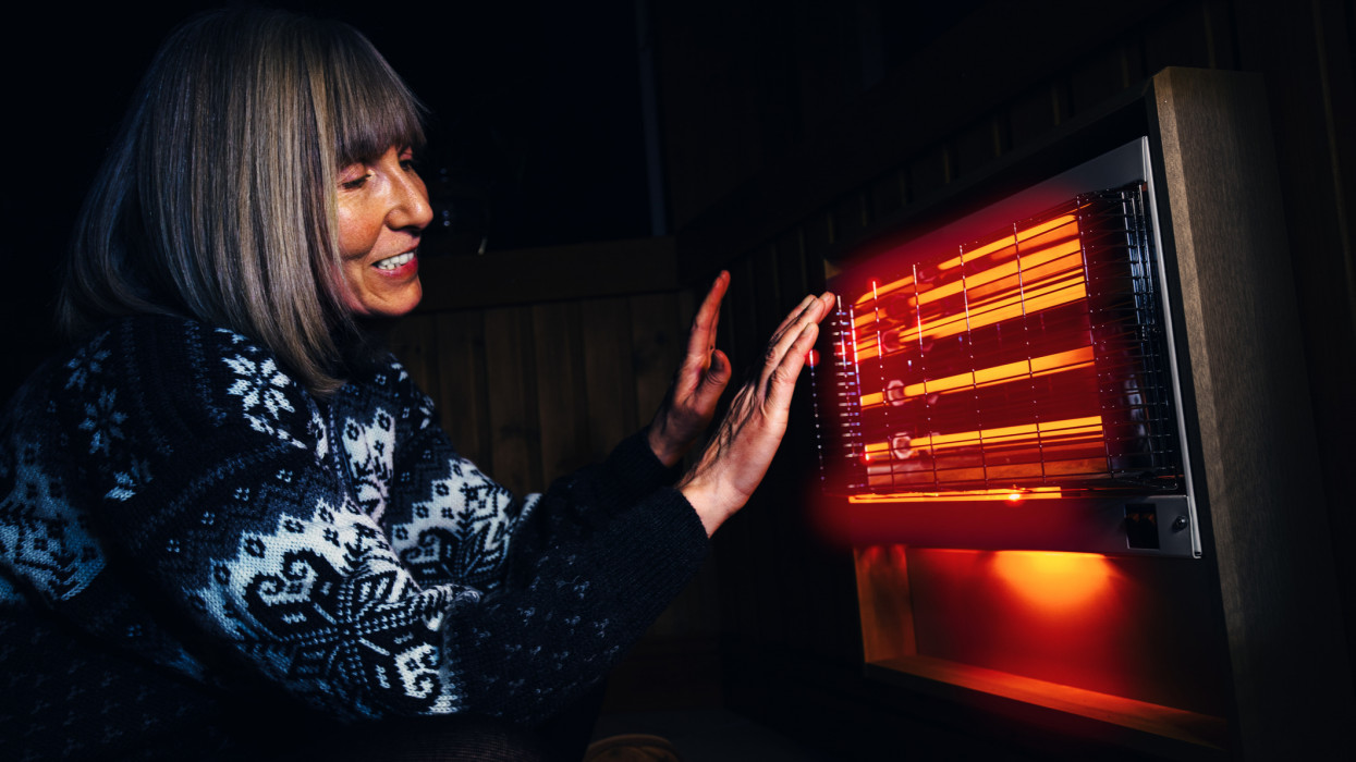 Mature woman warming her hands with the satisfying infrared rays of an electric bar fire.