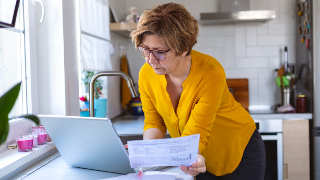 Concentrated mature woman calculating finance, money, using laptop computer at home , counting budget, paying bills, taxes, rent, mortgage fees