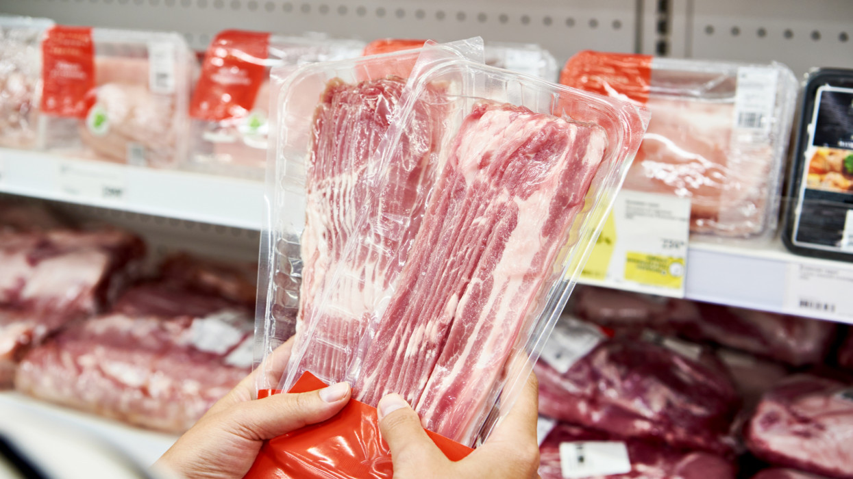 Woman chooses a slice of pork meat in vacuum package at the grocery store bacon store