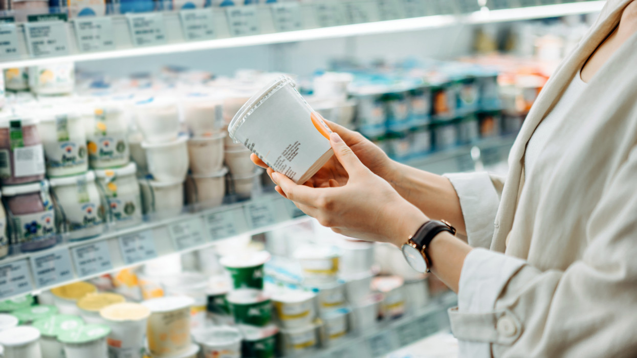 Cropped shot of young Asian woman shopping in the dairy section of a supermarket. She is reading the nutrition label on a container of fresh organic healthy natural yoghurt