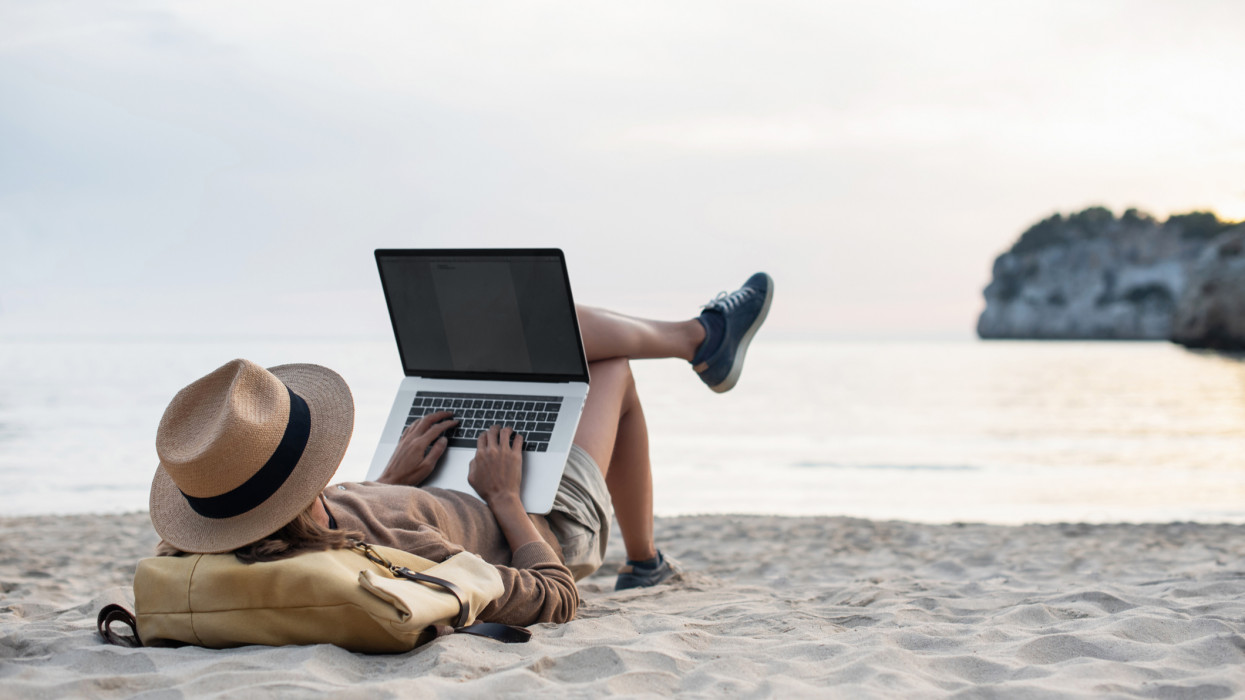 Woman working remote by the sea, has meeting online, using computer to plan trip, check in to hotels and flights, staying connected to friends, family and office. Freelance business concept