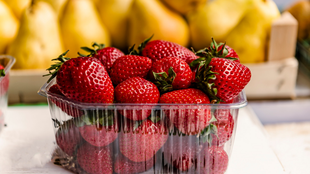 Close-up View at the Fresh and Delicious Strawberries in the Baskets and the Yellow Pears at the Farmers Market. The Garden Strawberry is a Widely Grown Hybrid Species of the Genus Fragaria.