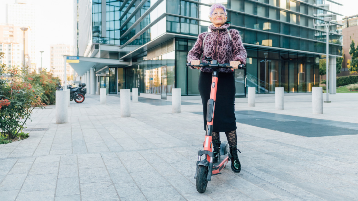 Italy, Fashionable senior woman on push scooter in city