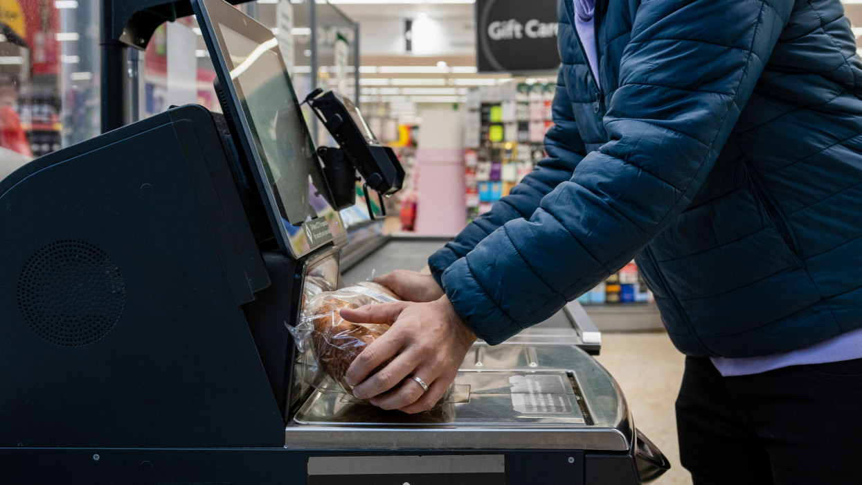 Side view of a man shopping in a supermarket while on a budget. He is scanning his items at the self service checkout in the North East of England.