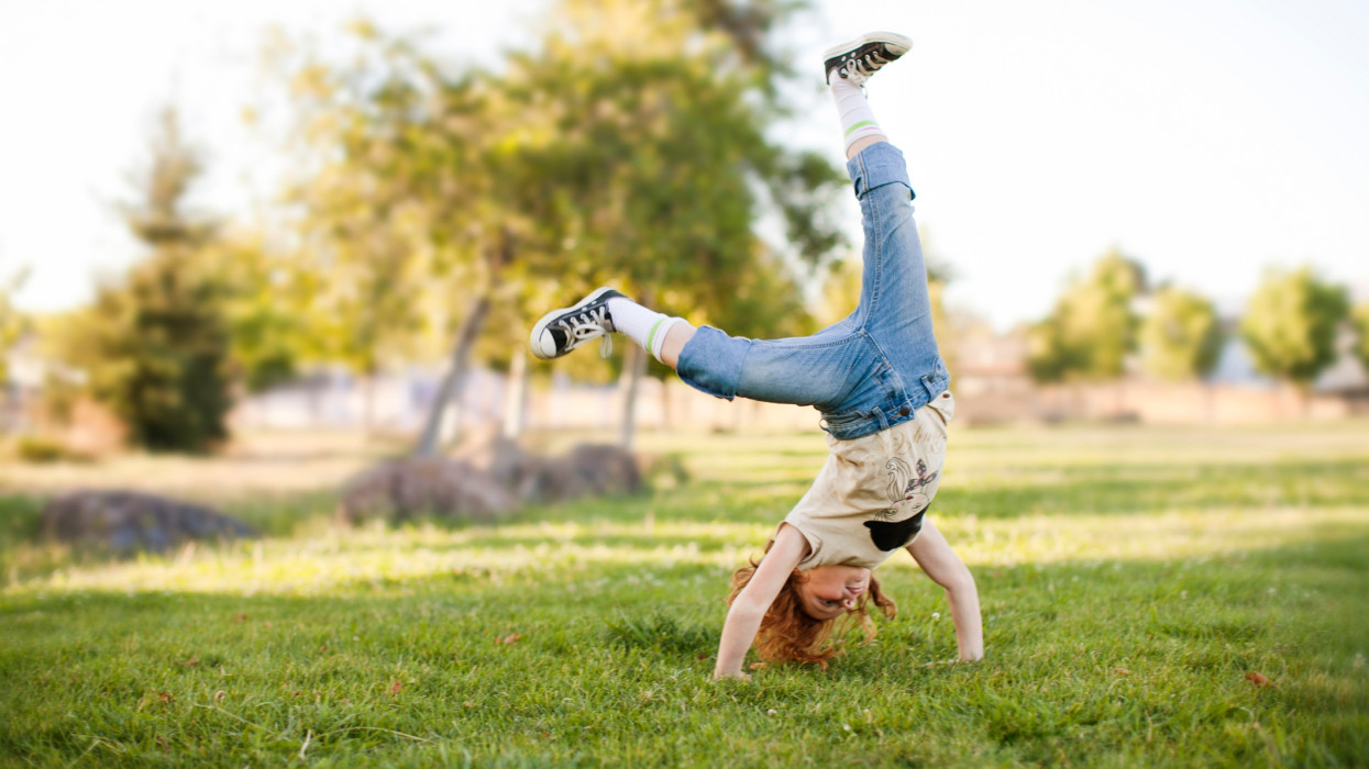 Young girl does cartwheel on the grass. She is mid hand stand.