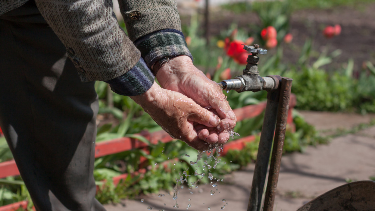 Senior adult washing hands in the garden tap water well