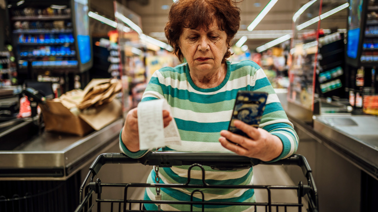 Senior woman with a smartphone checking the bill after shopping at the supermarket
