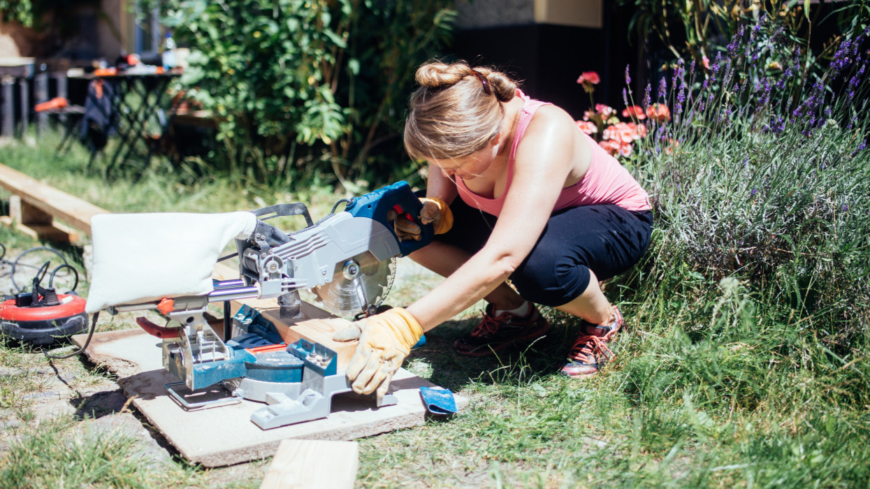 Woman building garden deck using a electric miter saw.