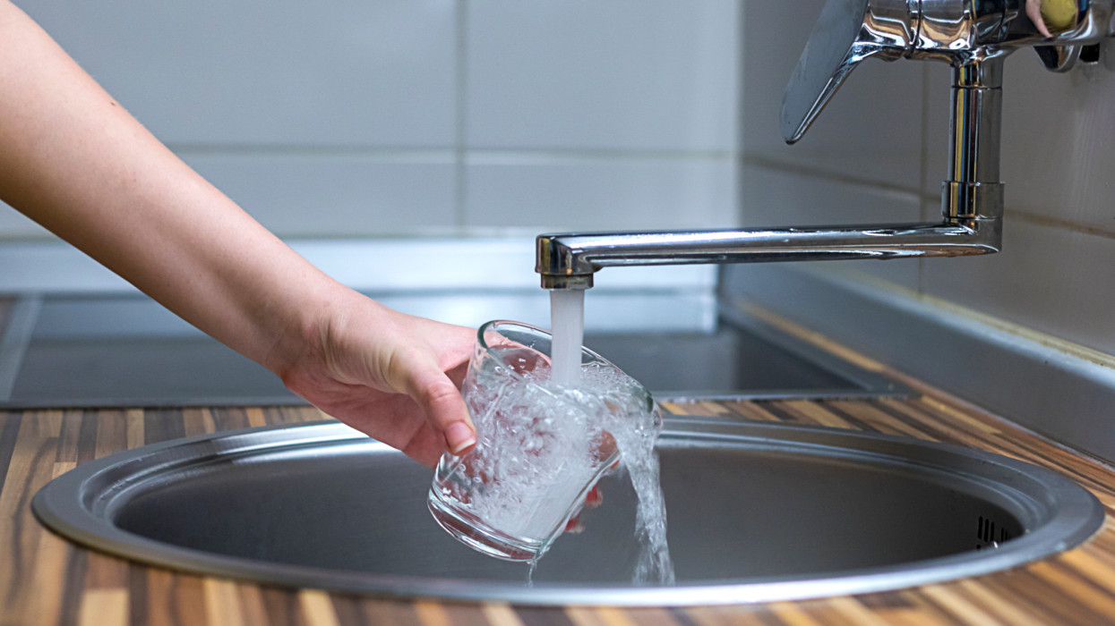 Female hands pouring water in glass cup from a kitchen faucet. Woman hands filling the glass of water. Filling glass of water from stainless steel kitchen faucet
