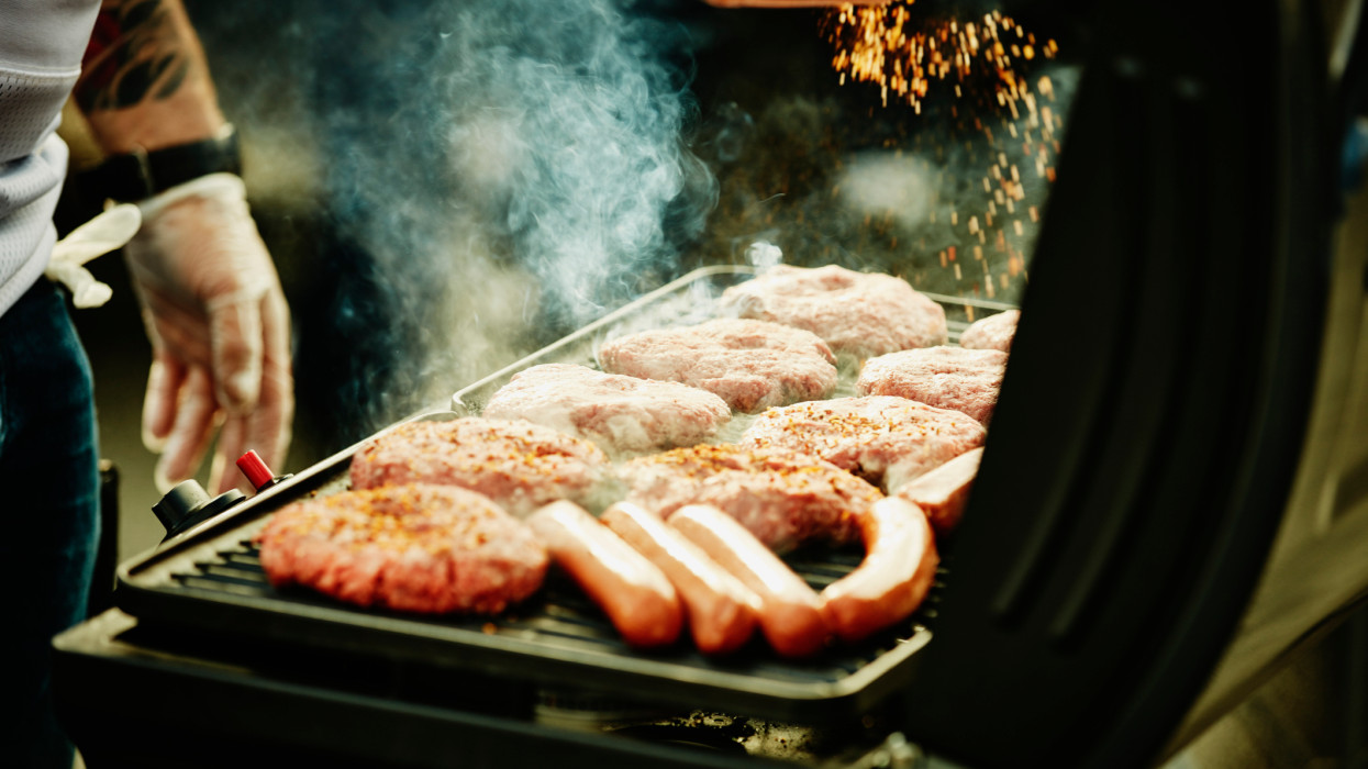 Man seasoning burgers and hot dogs on barbecue during tailgating party