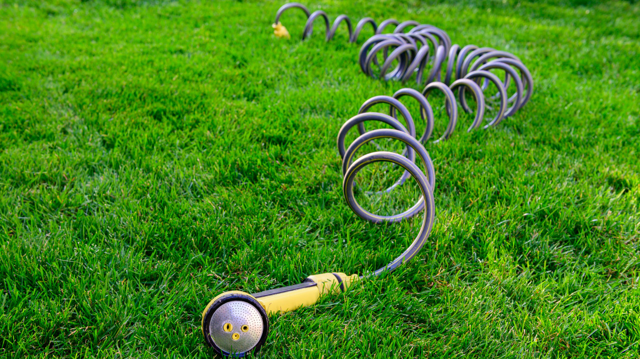 Garden Spray Nozzle, lying in the higher grass of the garden, after watering the lawn properly on a dry day stock photo