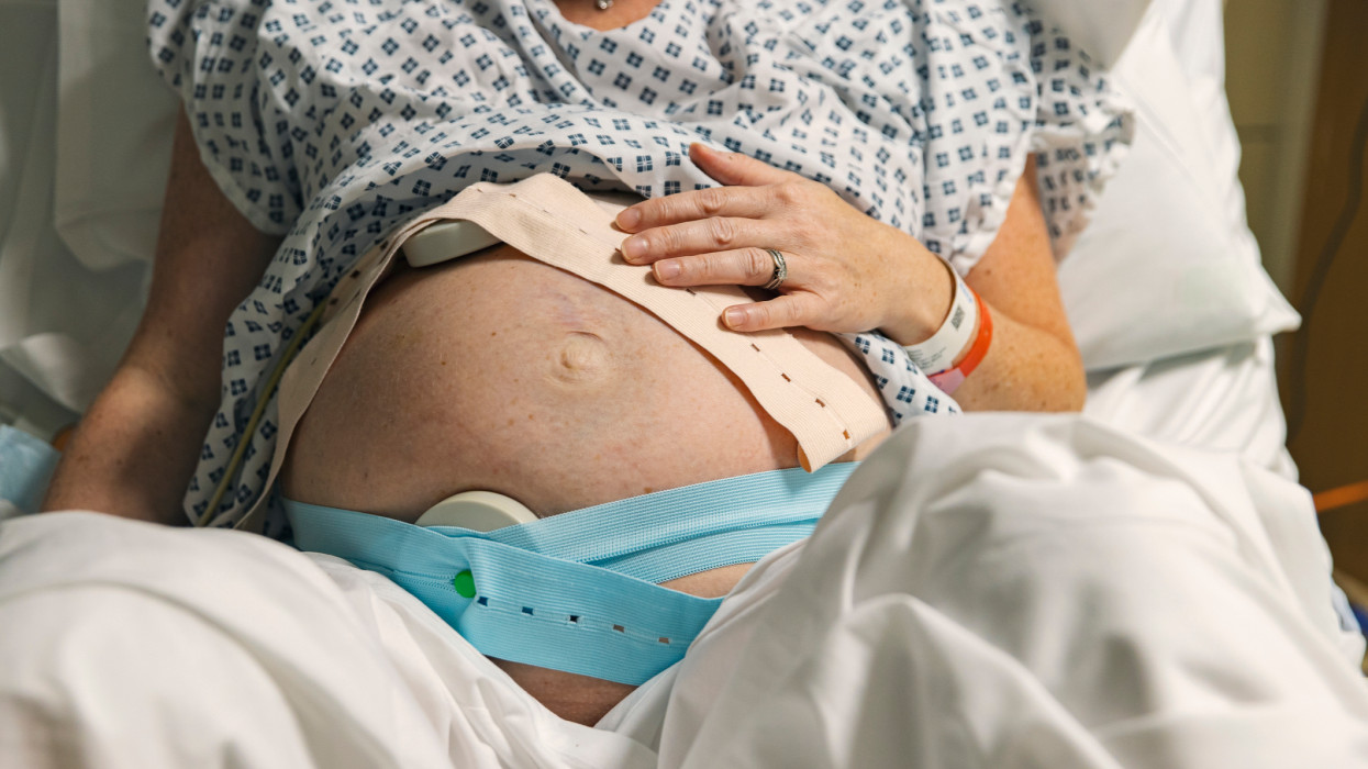 An unrecognisable mature pregnant woman lies on a hospital delivery bed as she has fetal monitoring. Cardiotocography is usually called a CTG by medical staff. It can be used to monitor a babys heart rate and a mothers contractions during pregnancy