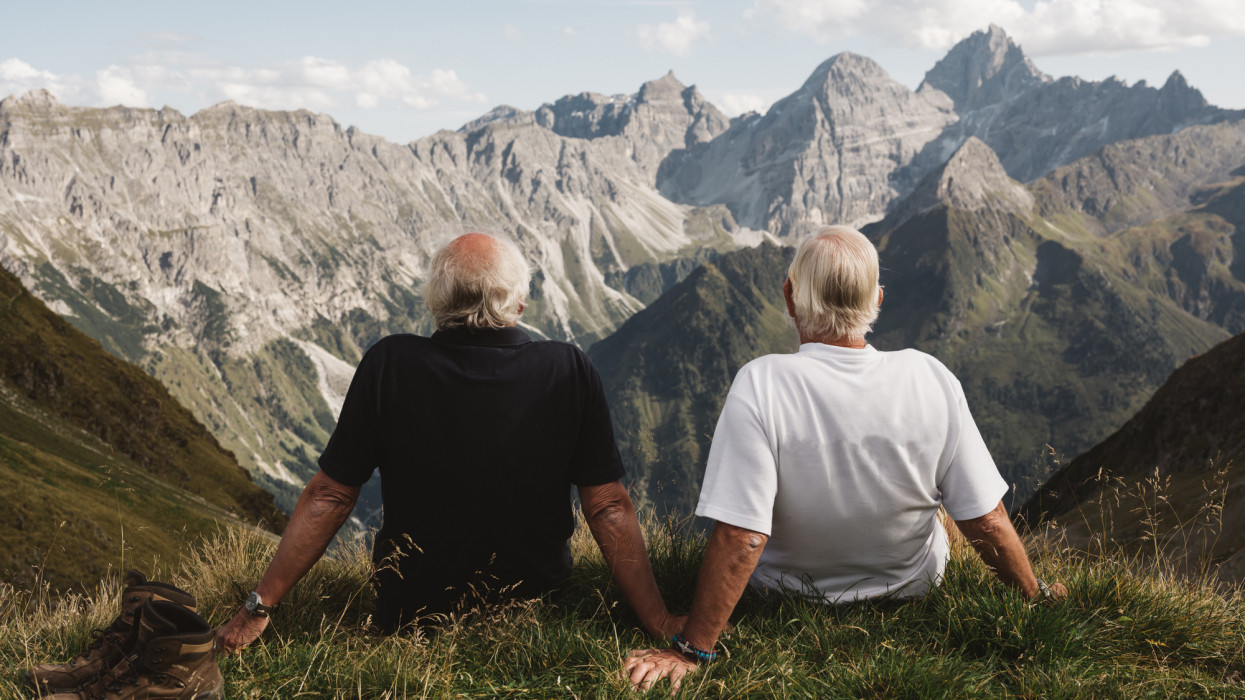 two seniors hikers sit and admire the view with rolling mountain tops in the distance