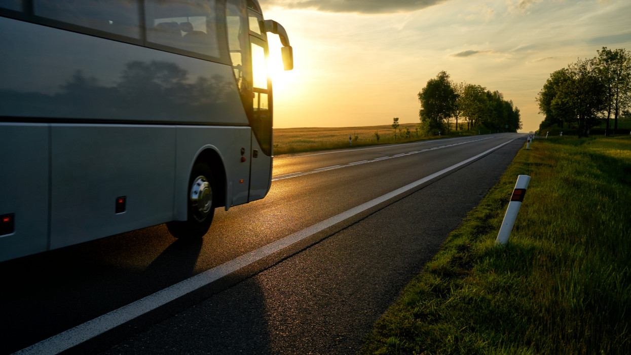 White Bus driving along the asphalt road in a rural landscape at sunset.