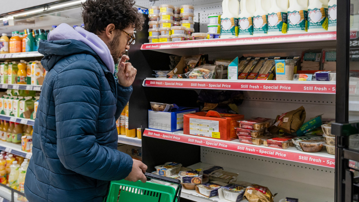 Man shopping in a supermarket while on a budget. He is looking for low prices due to inflation. He is living in the North East of England, browsing in the reduced section.